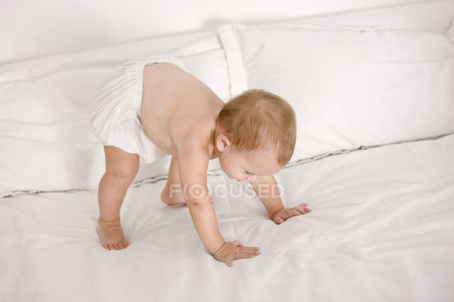 Малышка пытается встать на кровать — стоковое фото