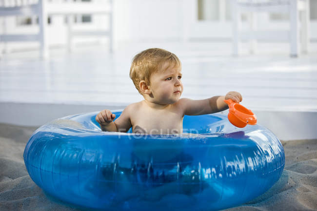 Baby boy sitting in inflatable ring and looking away — Stock Photo