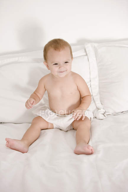 Милая малышка улыбается на кровати и смотрит в сторону — стоковое фото