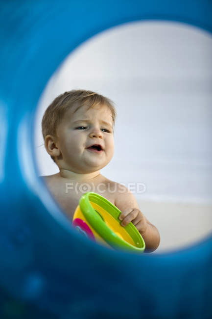 Baby boy playing with toy viewed through inflatable ring — Stock Photo