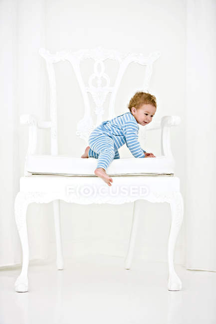 Улыбающийся мальчик вылезает из огромного белого кресла — стоковое фото