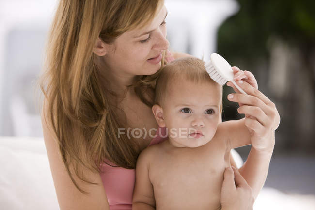 Woman brushing baby daughter hair — Stock Photo