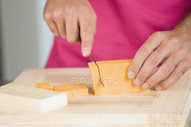 Close-up de mãos masculinas corte de fatias de queijo em tábua de corte de madeira — Fotografia de Stock
