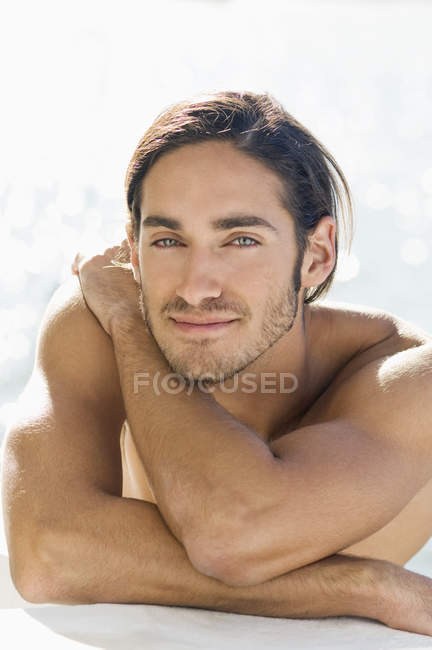 Portrait of sensual shirtless young man leaning on elbows at sea water — Stock Photo