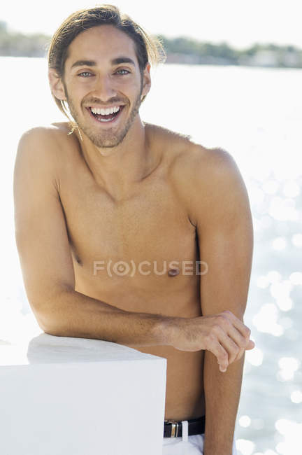 Portrait of smiling shirtless young man standing at lake shore — Stock Photo