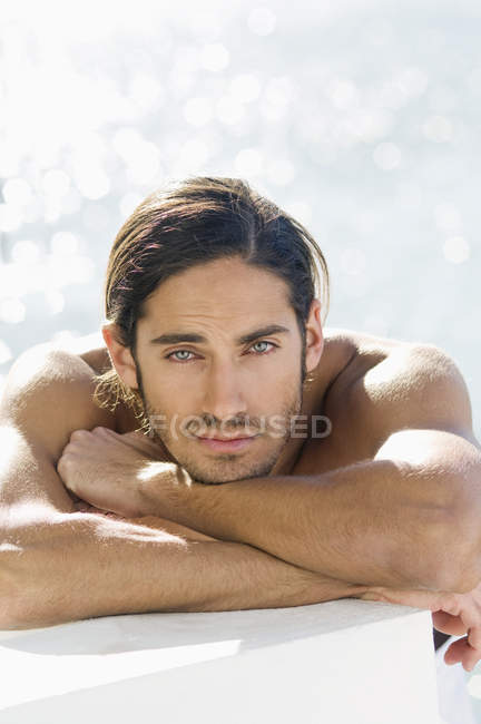 Porträt eines sinnlichen, hemdlosen jungen Mannes, der sich auf Ellbogen am Meerwasser lehnt — Stockfoto