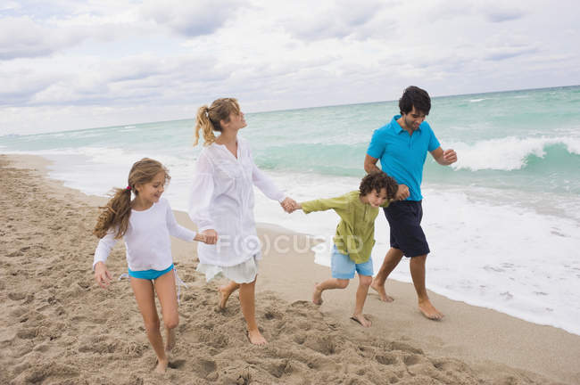 Familia feliz corriendo en la playa de arena - foto de stock