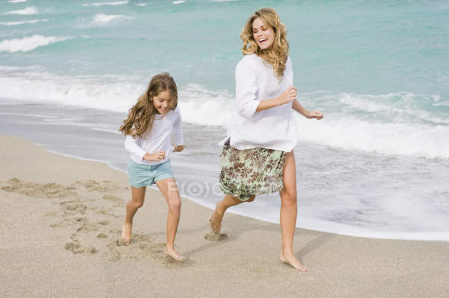 Жінка біжить з дочкою на піщаному пляжі — стокове фото
