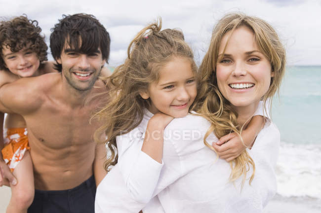 Casal dando piggyback passeio crianças na praia — Fotografia de Stock