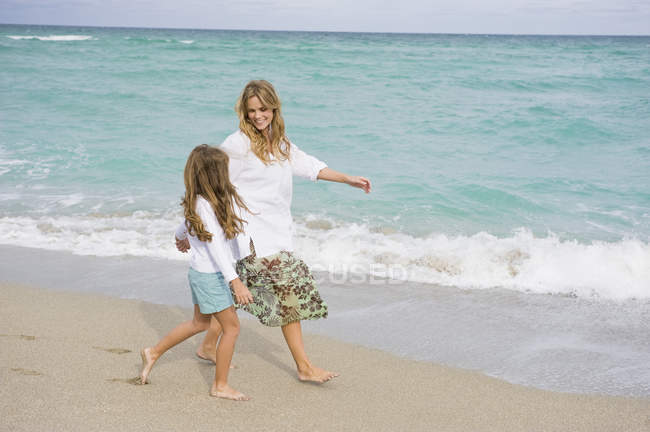 Mujer caminando en la playa de arena con su hija - foto de stock