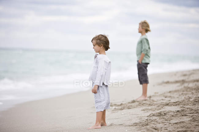 Boys standing on sandy beach in overcast and looking at view — Stock Photo