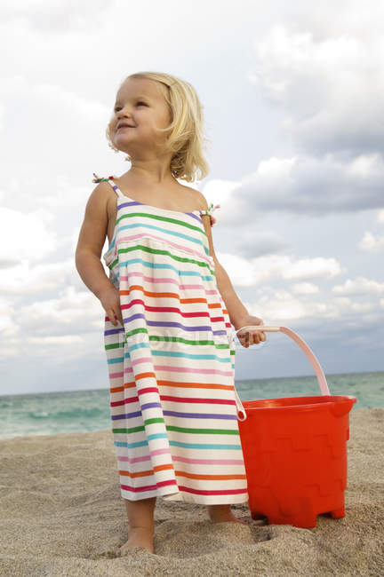 Menina bonito segurando balde de areia na praia — Fotografia de Stock
