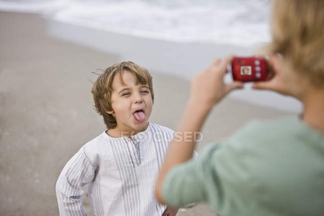 Menino tirando foto de irmão com câmera digital na praia — Fotografia de Stock