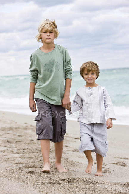Retrato de niños caminando por la playa tomados de la mano - foto de stock