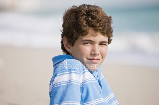 Retrato de menino sorridente sentado na praia — Fotografia de Stock