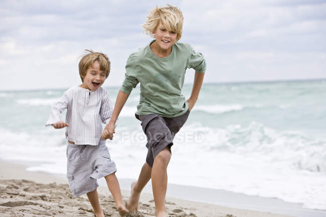 Meninos alegres correndo na praia arenosa — Fotografia de Stock