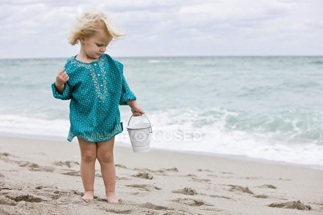 Menina segurando balde de areia na praia — Fotografia de Stock