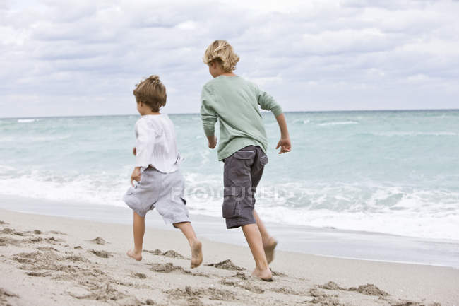Вид на веселых мальчишек, бегущих по песчаному пляжу — стоковое фото