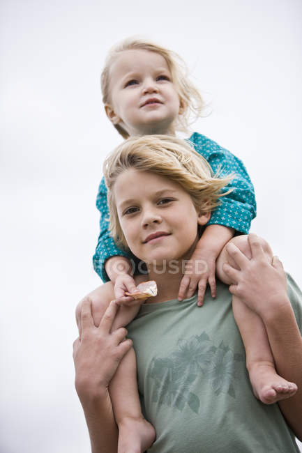 Boy carrying sister on shoulders on beach — Stock Photo