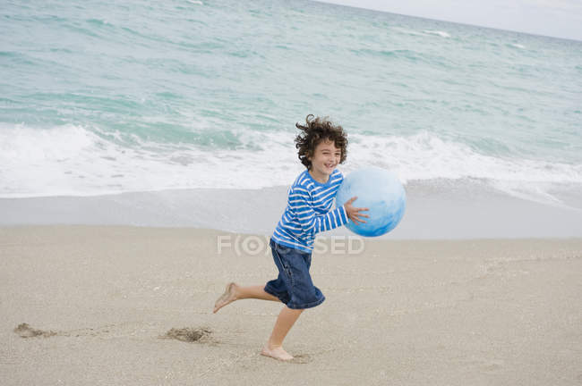 Веселий хлопчик грає з м'ячем на пляжі — стокове фото