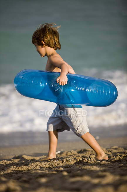 Niño pequeño llevando anillo inflable en la playa - foto de stock