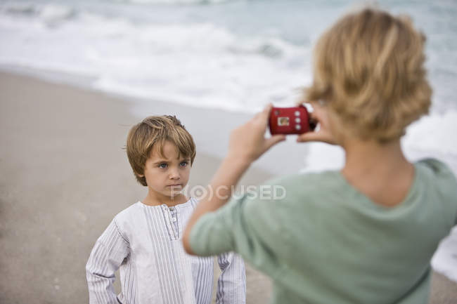 Мальчик фотографирует брата с цифровой камерой на пляже — стоковое фото