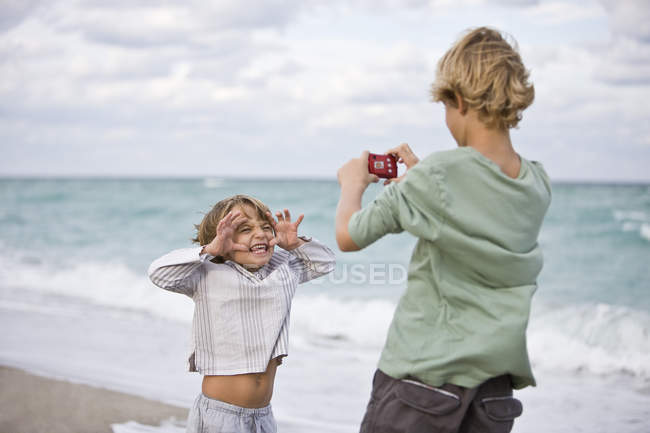 Хлопчик фотографує брата з цифровою камерою на пляжі — стокове фото