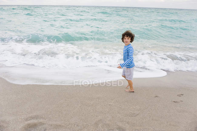 Ragazzo con i capelli ricci in piedi sulla spiaggia e guardando altrove — Foto stock