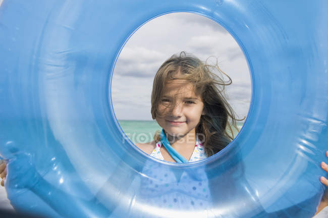 Girl looking through inflatable ring on beach — Stock Photo