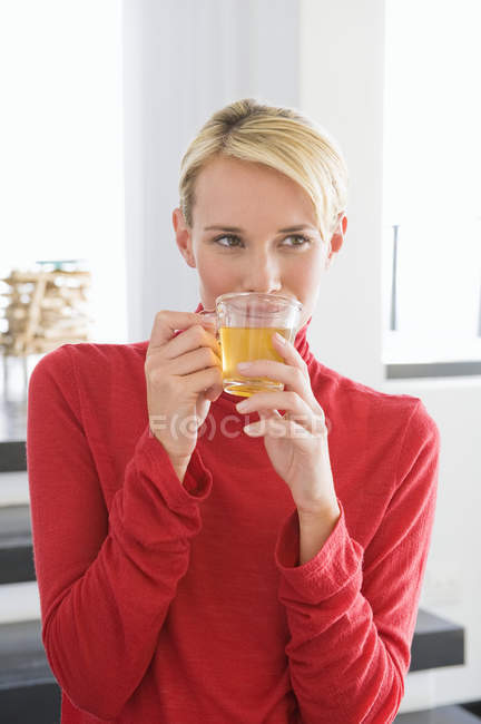 Jovem mulher em pulôver vermelho segurando xícara de chá — Fotografia de Stock