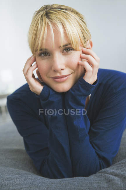 Smiling dreamy woman lying on bed and leaning on elbows — Stock Photo