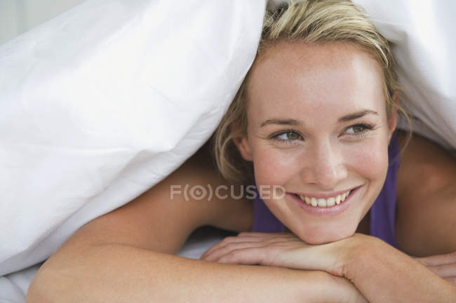 Крупним планом жінка лежить на ліжку під ковдрою і посміхається — стокове фото
