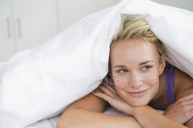 Close-up de mulher deitada na cama sob edredão e sorrindo — Fotografia de Stock