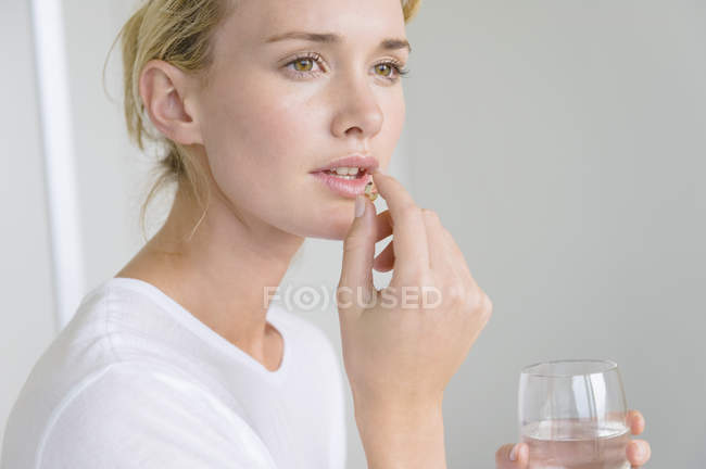 Mujer que toma la cápsula Omega-3 y sostiene el vaso de agua - foto de stock