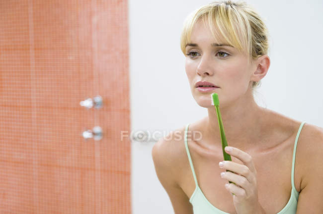 Riflessione della donna in specchio che tiene lo spazzolino da denti — Foto stock