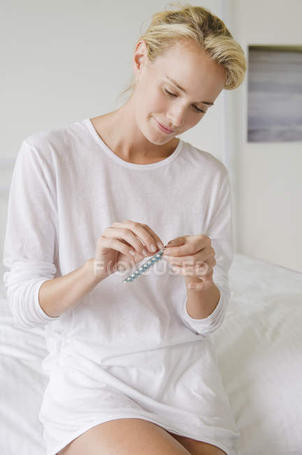 Mulher segurando embalagem blister de medicamento enquanto está sentada na cama — Fotografia de Stock