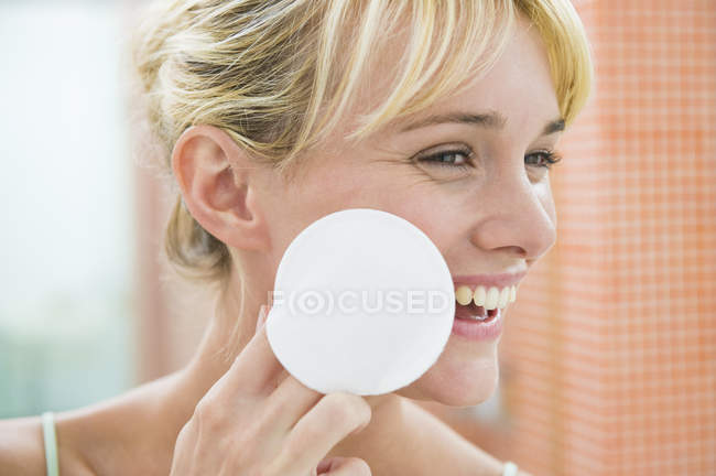 Смеющаяся женщина наносит порошок для лица ватным шариком — стоковое фото