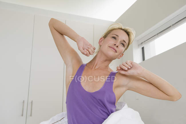 Lächelnde junge Frau, die sich morgens auf dem Bett ausstreckt — Stockfoto