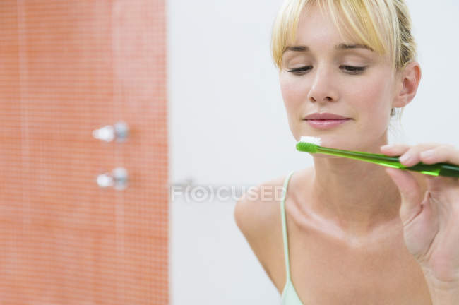 Reflexão da mulher no espelho segurando escova de dentes — Fotografia de Stock