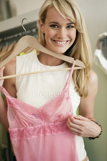 Sorrindo jovem segurando vestido rosa enquanto faz compras na boutique — Fotografia de Stock