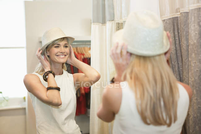 Charming blond woman trying on fedora in fashion boutique — Stock Photo