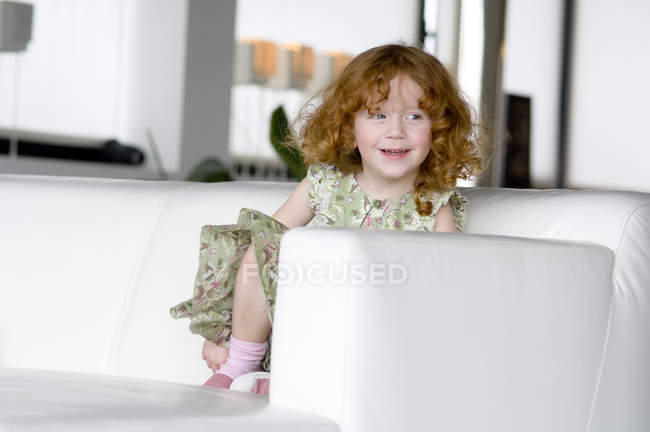 Ritratto della piccola ragazza rossiccia seduta su un divano — Foto stock