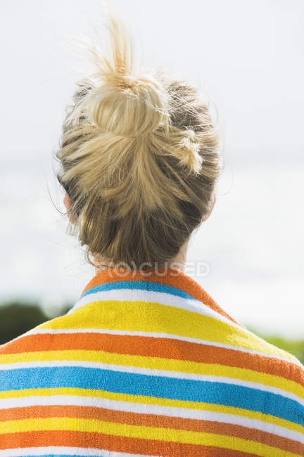 Visão traseira da mulher com toalha de praia listrada colorida em torno dos ombros — Fotografia de Stock