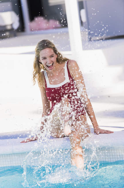 Allegro giovane donna seduta a bordo piscina e spruzzi d'acqua — Foto stock