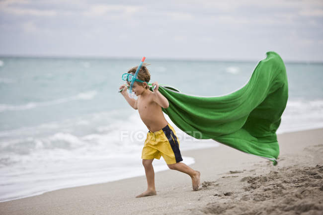 Мальчик в маске с аквалангом бегает по пляжу с зеленым парео — стоковое фото