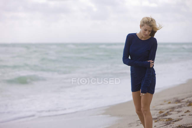 Femme blonde réfléchie en robe debout sur la plage venteuse — Photo de stock