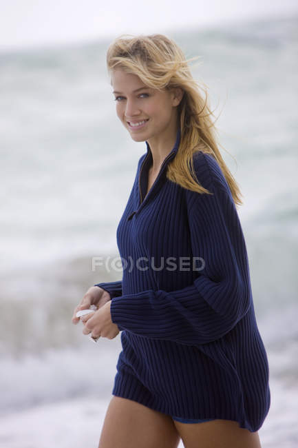 Femme souriante tenant coquille tout en marchant sur la plage — Photo de stock