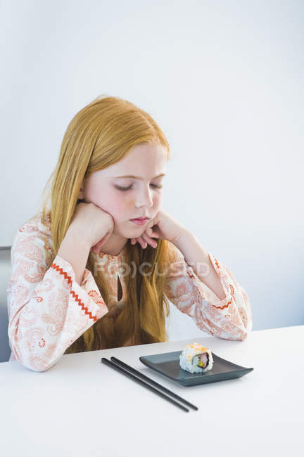 Trauriges Ingwermädchen sitzt am Esstisch und betrachtet Sushi — Stockfoto