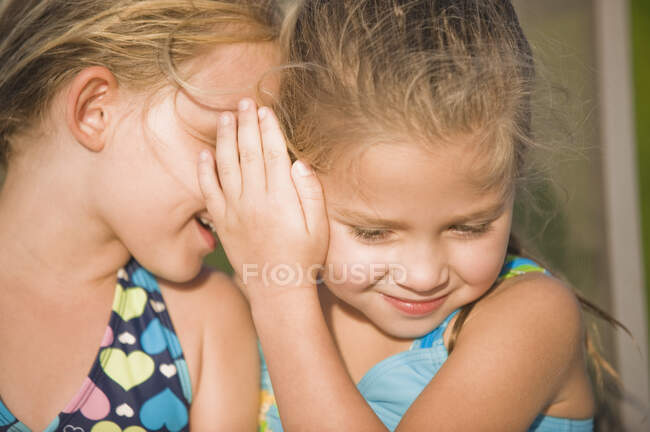 Girl whispering into her friend's ear — Stock Photo
