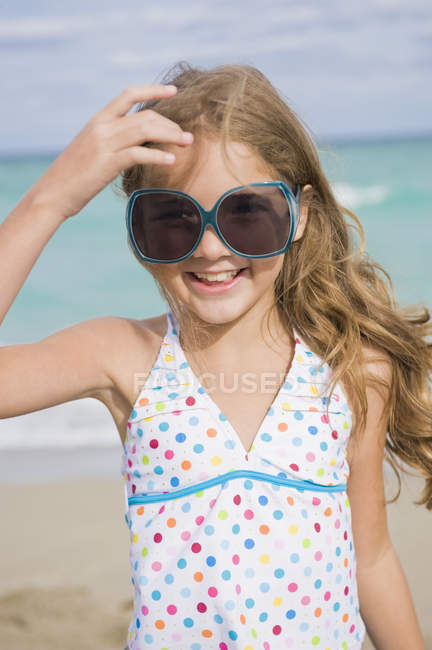 Смолящая маленькая девочка в платье и солнцезащитных очках позирует на пляже — стоковое фото